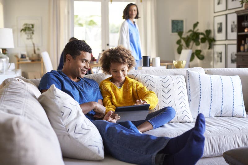 Schließen Sie oben vom jungen Vater, der auf Sofa im Wohnzimmer mit seiner jugendlichen Tochter sitzt, die Tablet-Computer, selek stockbild Schließen Sie oben vom jungen Vater, der auf Sofa im Wohnzimmer mit seiner jugendlichen Tochter sitzt, die Tablet-Computer, selek stockbild