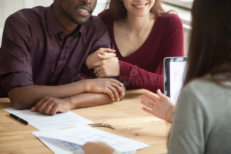 Close up of happy multiracial couple buying home together form female real estate agent. Caucasian wife supports African American husband in successful investment. Concept of new home purchase. Close up of happy multiracial couple buying home together form female real estate agent. Caucasian wife supports African American husband in successful investment. Concept of new home purchase