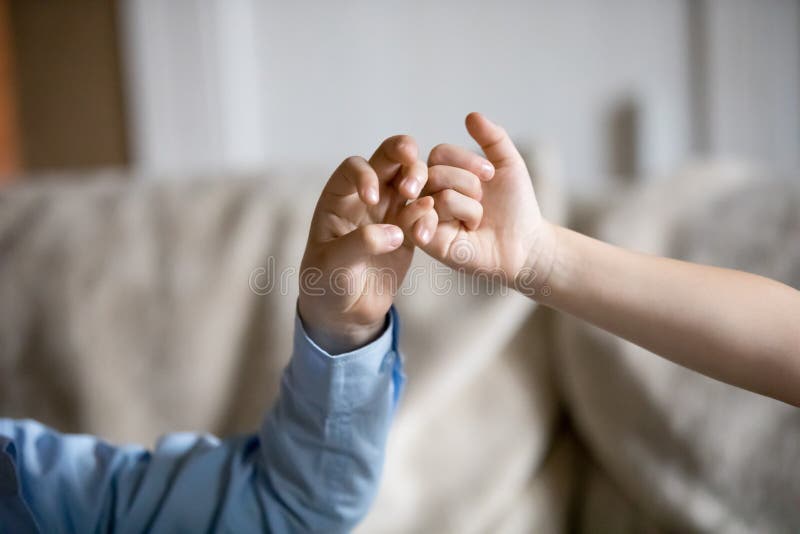 Schließen Sie oben von den Kinderhänden, die Versprechen des kleinen Fingers machen. Abschluss oben von kleinen Kindern versöhnen, nachdem der Kampf, der Versprechen des kleinen Fingers macht, Kinder Frieden mit den Verbindungskleinen fingern des Handzeichens schwören lassen, um nicht zu argumentieren oder Streit, Geschwister stehen Freunden Portrait von zwei nassen Pelikanen auf dunklem Hintergrund