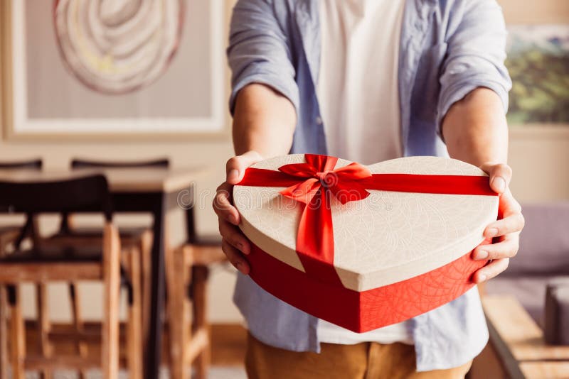 Schließen Sie oben von den Mannhänden, die ein anwesendes Geschenk in Richtung zur Kamera geben - Feiertagsthema - im warmen Sonn Schließen Sie oben von den Mannhänden, die ein anwesendes Geschenk in Richtung zur Kamera geben - Feiertagsthema - im warmen Sonn