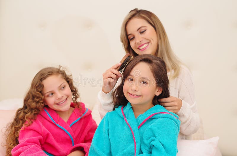 Schließen Sie oben von der jungen Mutter, die das Haar ihres wenig daugher brussing ist, das ein blaues bathtowel während ihr and stockfoto
