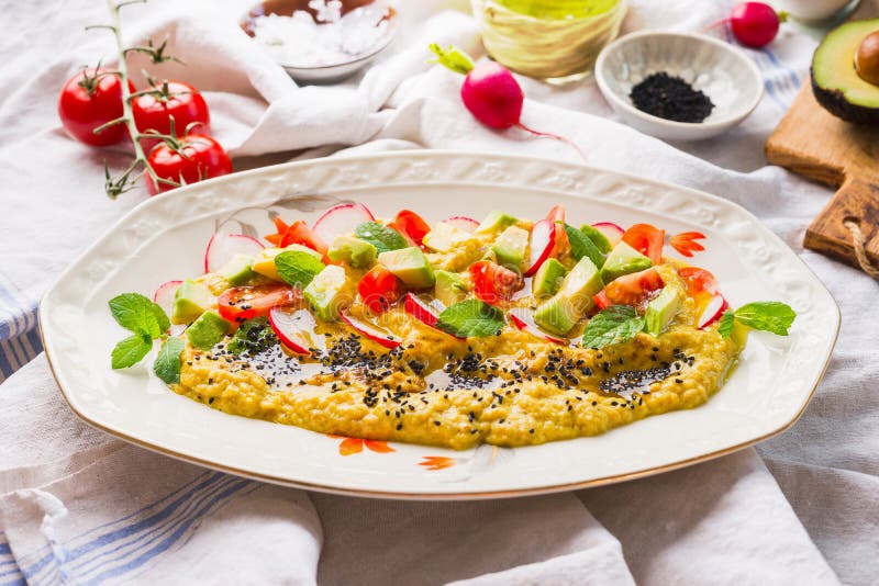Schließen Sie oben von hummus Platte, die mit dem Olivenöl, Avocado, Frischgemüse und den Kräutern gedient werden auf Küchentisch lizenzfreies stockbild Schließen Sie oben von hummus Platte, die mit dem Olivenöl, Avocado, Frischgemüse und den Kräutern gedient werden auf Küchentisch lizenzfreies stockbild