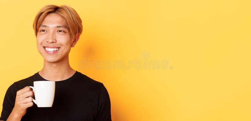Schließung eines glücklich ansehenden jungen Asiaten mit blonden Haaren, der träumlich aussieht und beim Kaffee oder Tee lächelt stockbilder