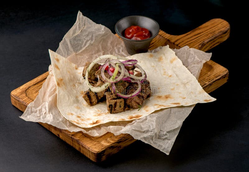 Schließung von gegrilltem Rindfleisch mit Pita-Brot und Zwiebeln auf dunklem Hintergrund. Fleisch auf Holzbrett lizenzfreie stockbilder