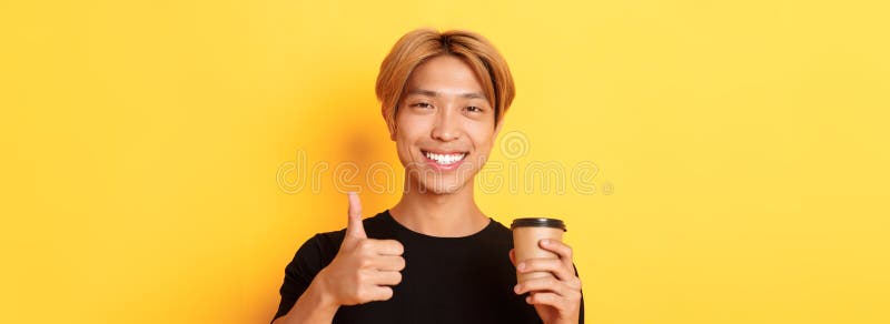 Schließung von zufriedenen asiatisch ansehnlichen Kerl empfehlen Café halten Tasse Kaffee und zeigen Daumen in Genehmigung stockfoto