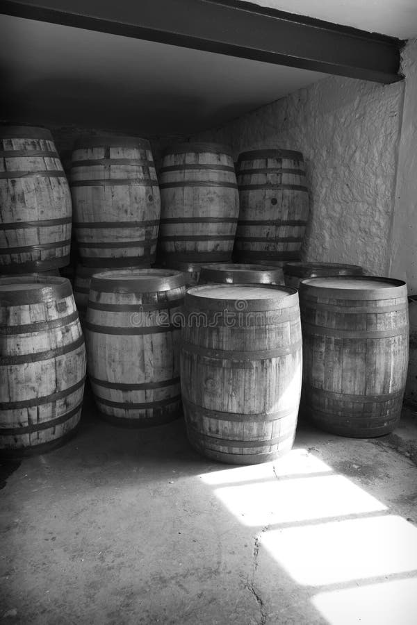 Schlussleuchten und weiße alte Whiskyfässer gestapelt in einem Lager bereit, mit rohem Geist zu füllen und zu gehen, um in einem s. Alte Whiskyschwarzweiss-fässer gestapelt in einem Lager bereit, mit rohem Geist zu füllen und zu gehen, um in einem staubigen Lager mit dem hellen Hinaufklettern durch ein Fenster im Laufe der Zeit reifen