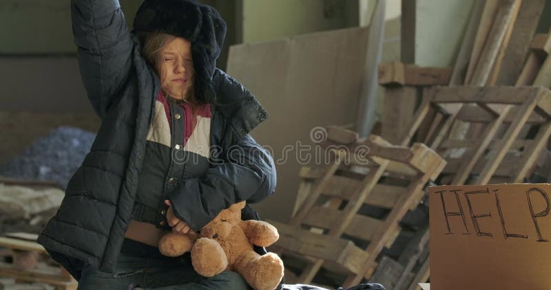 Schläfriges kaukasisches Mädchen in Winterbekleidung sitzt mit dem Teddybär auf der Baustelle Erschöpftes Kind