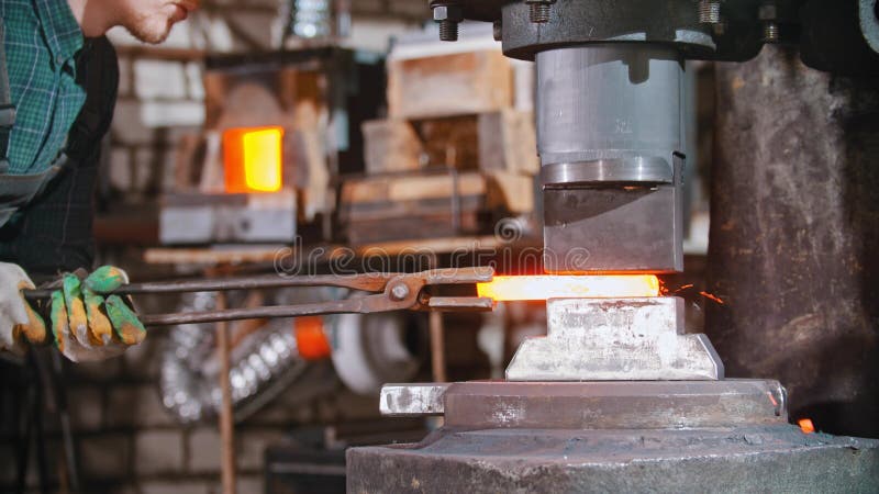 Schmied, der ein längeres Stück Metall unter dem Druck der Industrie schmiedenden Maschine Aussetzen funktioniert