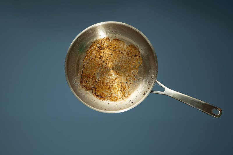 Dirty oily burnt metal frying pan or skillet isolated on a light blue background, no people. Dirty oily burnt metal frying pan or skillet isolated on a light blue background, no people.