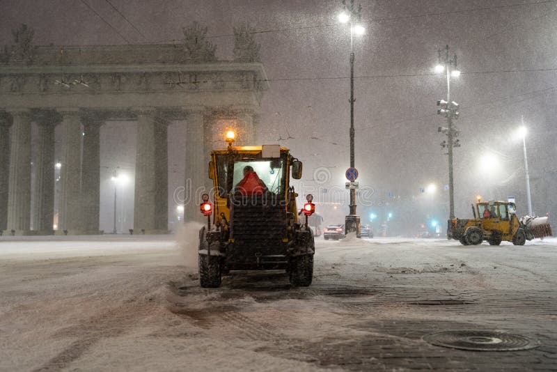 Snow removal equipment work in city after snowfall. Tractors, bulldozers and snowblowers cleaning streets, roads and squares in night during wintertime blizzard storm. Snowy winter in Russia concept. Snow removal equipment work in city after snowfall. Tractors, bulldozers and snowblowers cleaning streets, roads and squares in night during wintertime blizzard storm. Snowy winter in Russia concept