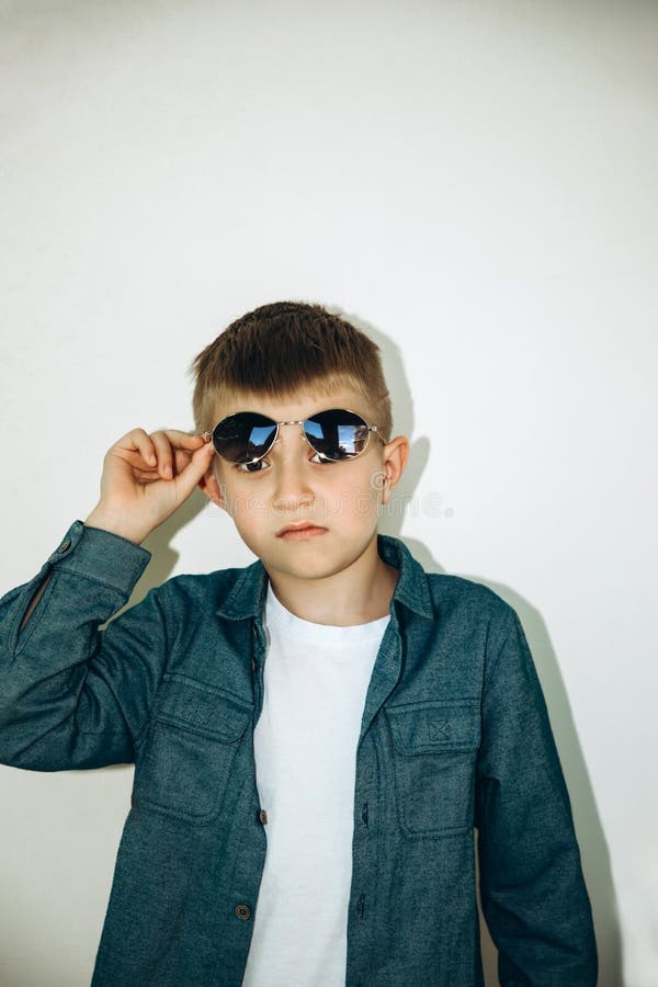 A School Age Boy In A Blue Shirt Lifts His Sunglasses And Smiles Stock