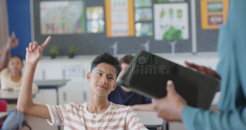 In school, boy raising hand in classroom, engaging with teacher stock video footage