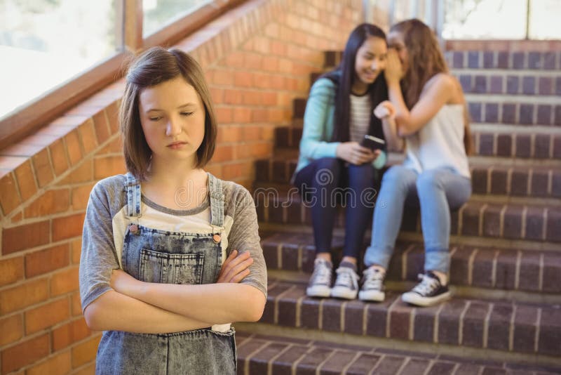 School friends bullying a sad girl in school corridor