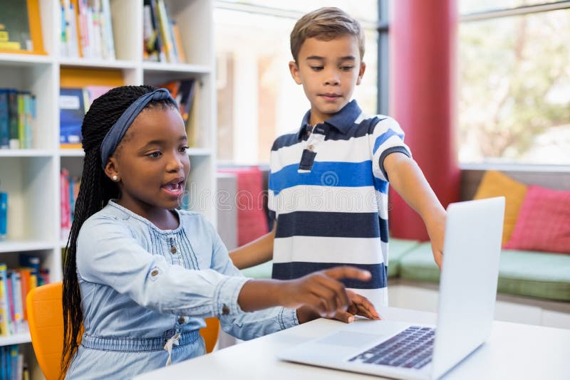 School kids using a laptop in library stock photography School kids using a laptop in library stock photography