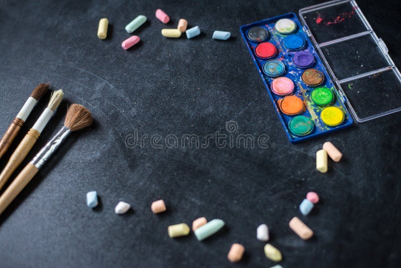 School and office supplies. Chalk scattered and paint brushes on the the old black board.