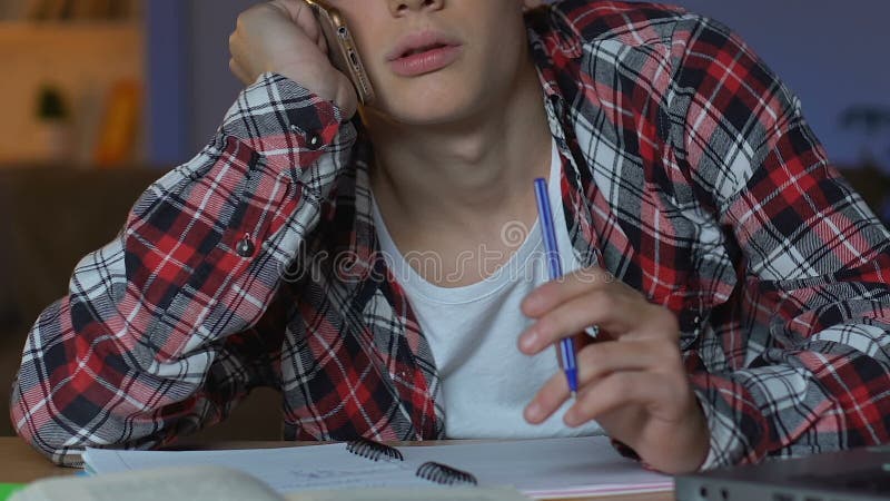 School pupil talking phone while doing homework, feeling bored, studying break