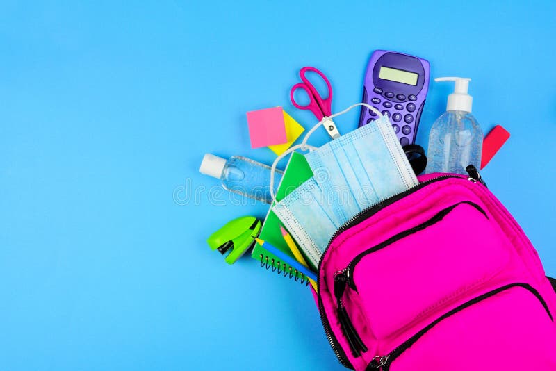 Backpack full of school supplies and COVID 19 prevention items. Top view, spilling onto a blue background. Back to school during p. Andemic concept