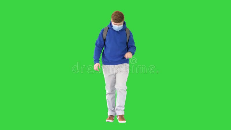 Schoolboy with backpack wearing medical mask walking on a Green Screen, Chroma Key.