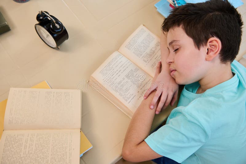 Schoolboy falling asleep on a textbook, feeling the fatigue doing homework. Difficulties in restoring the school regime stock image