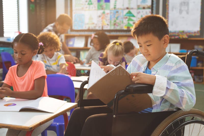 Side view of schoolboy studying in classroom while sitting at wheelchair in clasroom at school
