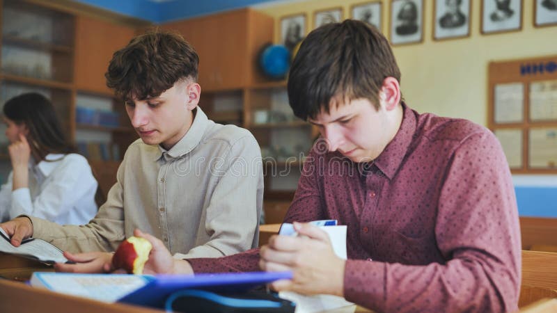 Schoolboys at a desk during class. The boy eats an apple. stock photos