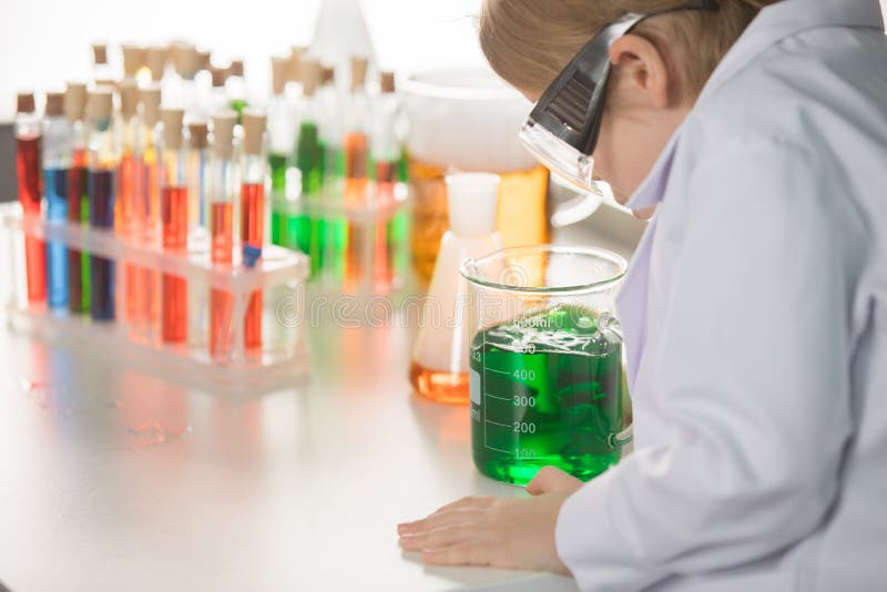 Schoolchild in Lab Coat and Protective Goggles Looking at Flask with ...