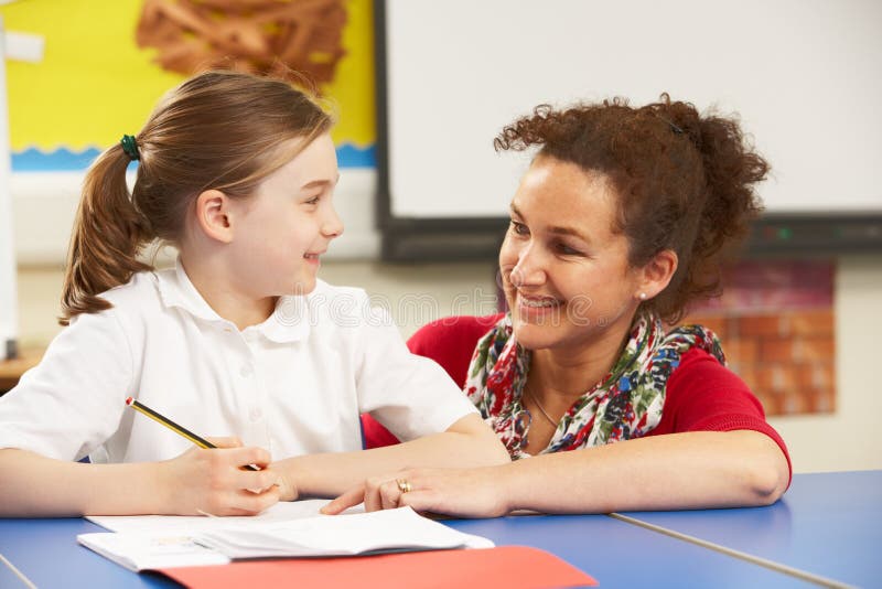 Schoolgirl Studying In Classroom With Teacher Smiling