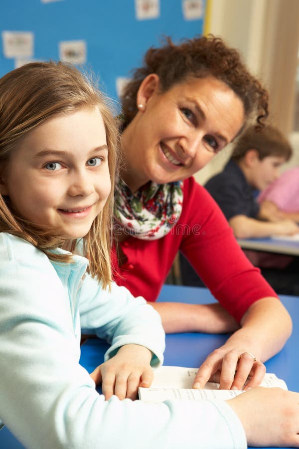 Schoolgirl Studying In Classroom With Teacher smiling at camera