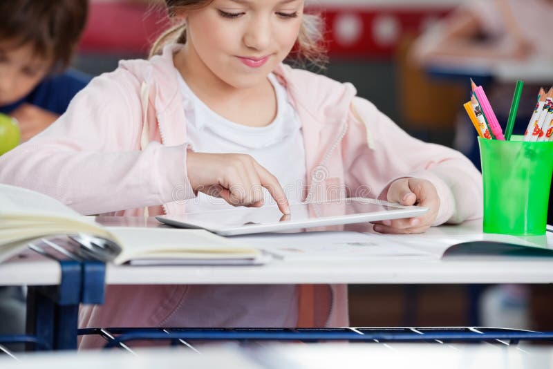 Little schoolgirl using digital tablet at desk in classroom. Little schoolgirl using digital tablet at desk in classroom