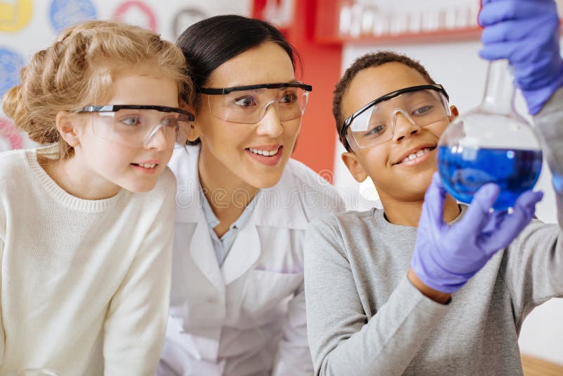 Schooljongen die fles met substantie tonen trots aan leraar en klasgenoot stock afbeelding Schooljongen die fles met substantie tonen trots aan leraar en klasgenoot stock afbeelding