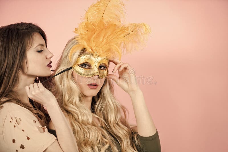 Woman put golden mask on girlfriend face. Girls with long hair on pink background. Fashion, beauty, look concept. Carnival, party, holidays, celebration. Love, lgbt, lesbian lifestyle romance. Woman put golden mask on girlfriend face. Girls with long hair on pink background. Fashion, beauty, look concept. Carnival, party, holidays, celebration. Love, lgbt, lesbian lifestyle romance