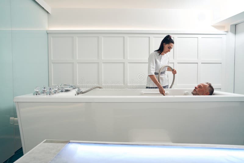 Man lying in white bathtub while having hydrotherapy procedure at wellness center. Man lying in white bathtub while having hydrotherapy procedure at wellness center