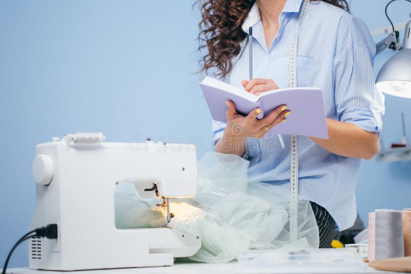 Schot van vrouw die nota's naast naaimachine maken stock foto Schot van vrouw die nota's naast naaimachine maken stock foto