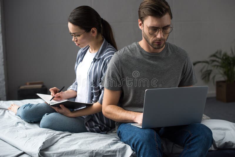 Schreiben des jungen Mannes und der Frau im Notizblock und Arbeiten an Laptop beim Sitzen stockbilder