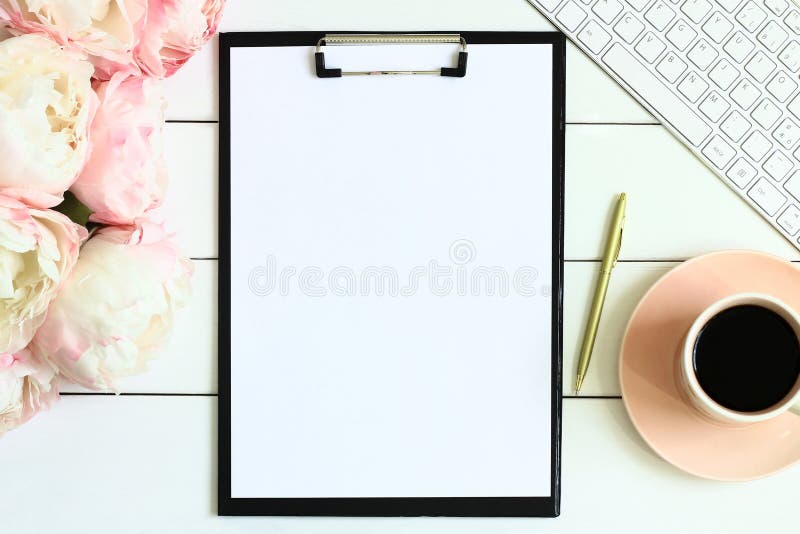 Schreibtischtabelle mit Tasse Kaffee, rosa Pfingstrosenblumen, goldenem Stift, leerem Papier und Klemmbrett stockfoto