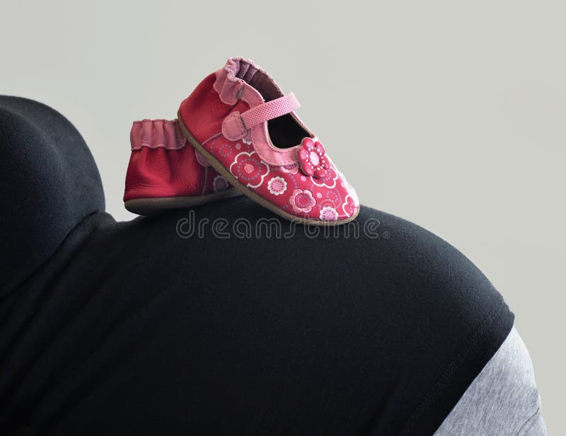 Schuhe für ein Baby auf dem Bauch eines schwangeres Mutter