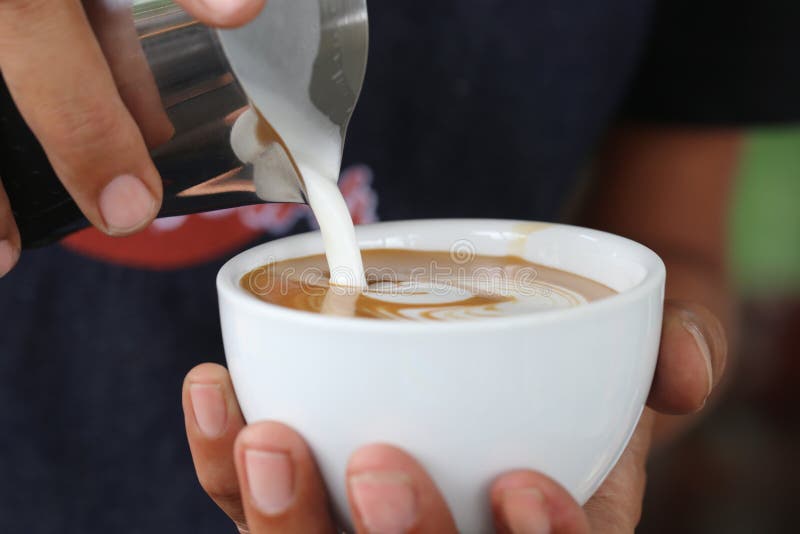Schuim van de Barista het gietende melk voor het maken van koffie latte tot kunst met patroon de bladeren in een kop
