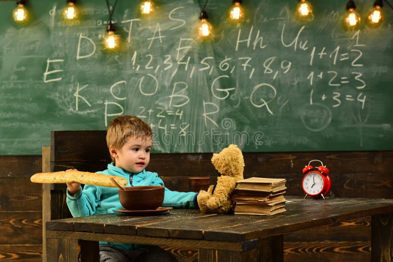 Schuljunge genießen Mittagspause mit Spielzeugfreund im Klassenzimmer Schuljunge essen Lebensmittel mit Teddybären betreffen Holz stockbild Schuljunge genießen Mittagspause mit Spielzeugfreund im Klassenzimmer Schuljunge essen Lebensmittel mit Teddybären betreffen Holz stockbild