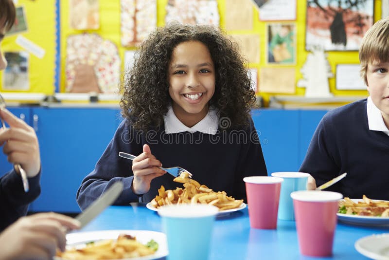 Schulkinder, die bei Tisch sitzen, das gekochte Mittagessen essend stockfotografie Schulkinder, die bei Tisch sitzen, das gekochte Mittagessen essend stockfotografie