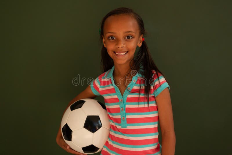 Schulmädchenstellung mit Fußball gegen grünes Brett in einem Klassenzimmer lizenzfreie stockfotografie Schulmädchenstellung mit Fußball gegen grünes Brett in einem Klassenzimmer lizenzfreie stockfotografie