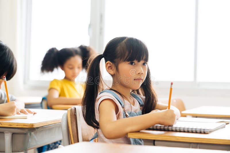 Schulmädchen, das im Schulschreiben im Buch mit einem Stift, Prüfung, Bildung sitzt und lernen Asiatische Kinder in der Klasse stockbild