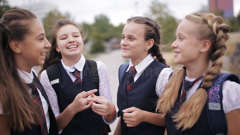 Schulmädchen, die den Spaß nach der Schule auf der Straße haben Studentin, welche die gleiche lachende und singende Schuluniform