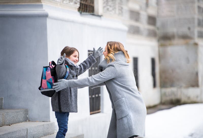 Schulmädchen grüßen umarmende Mutter vor dem Schulgebäude. AbholTochter aus der Grundschule. lizenzfreies stockfoto