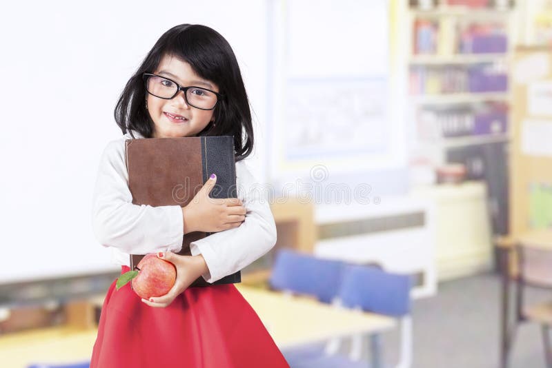 Schulmädchen hält Buch und Apfel in der Klasse lizenzfreie stockbilder Schulmädchen hält Buch und Apfel in der Klasse lizenzfreie stockbilder