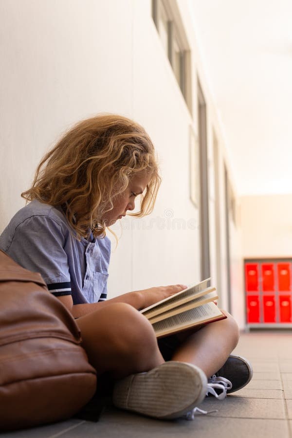 Schulmädchen mit der Schultasche, die auf Boden sitzt und ein Buch liest stockbild Schulmädchen mit der Schultasche, die auf Boden sitzt und ein Buch liest stockbild