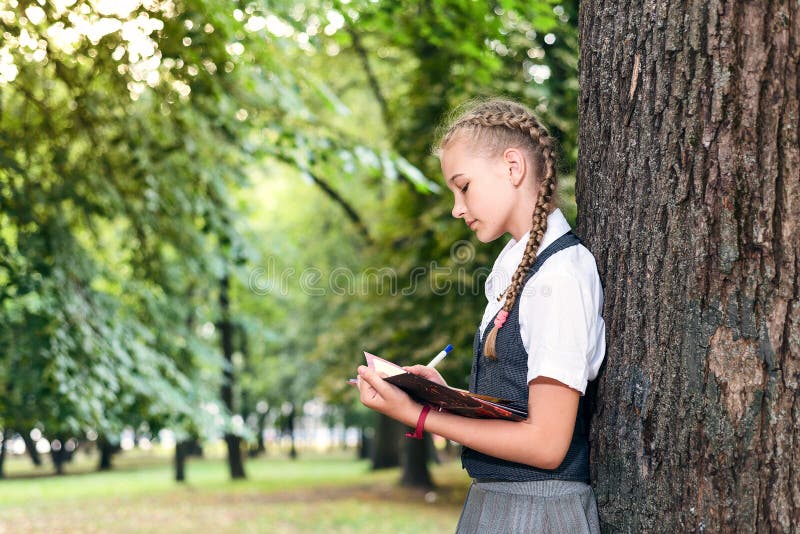 Schulmädchenjugendlicher, der ein Buch in einem Park nahe einem Baum liest lizenzfreie stockfotografie Schulmädchenjugendlicher, der ein Buch in einem Park nahe einem Baum liest lizenzfreie stockfotografie