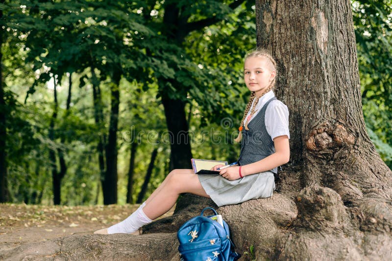 Schulmädchenjugendlicher, der ein Buch in einem Park nahe einem Baum liest lizenzfreie stockfotografie Schulmädchenjugendlicher, der ein Buch in einem Park nahe einem Baum liest lizenzfreie stockfotografie