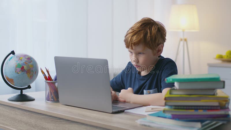 Schulungskonzept. niedlicher kleiner Junge, der auf dem Laptop tippt und mit Büchern und Globus zu Hause am Arbeitsplatz sitzt stock video footage