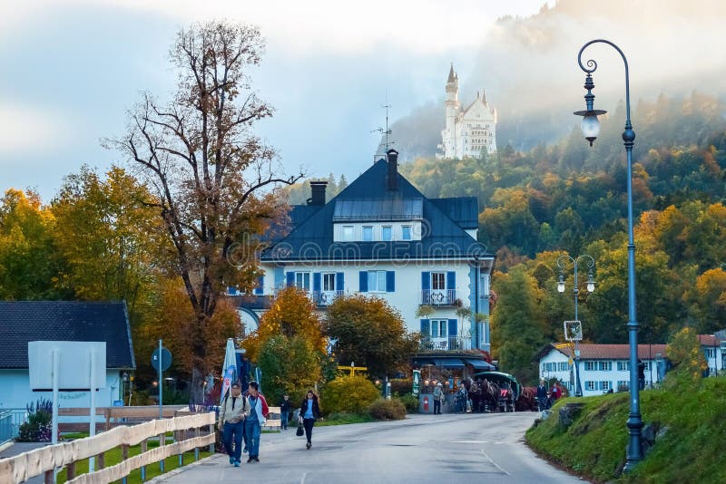 SCHWANGAU, DEUTSCHLAND - OKTOBER 09, 2018: Touristen auf der Straße der Altstadt mit Laternen und antiker Burg auf dem Hügel stockfoto SCHWANGAU, DEUTSCHLAND - OKTOBER 09, 2018: Touristen auf der Straße der Altstadt mit Laternen und antiker Burg auf dem Hügel stockfoto