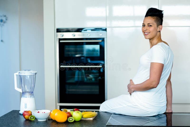 Pregnant woman sitting on kitchen worktop and smiling. Pregnant woman sitting on kitchen worktop and smiling